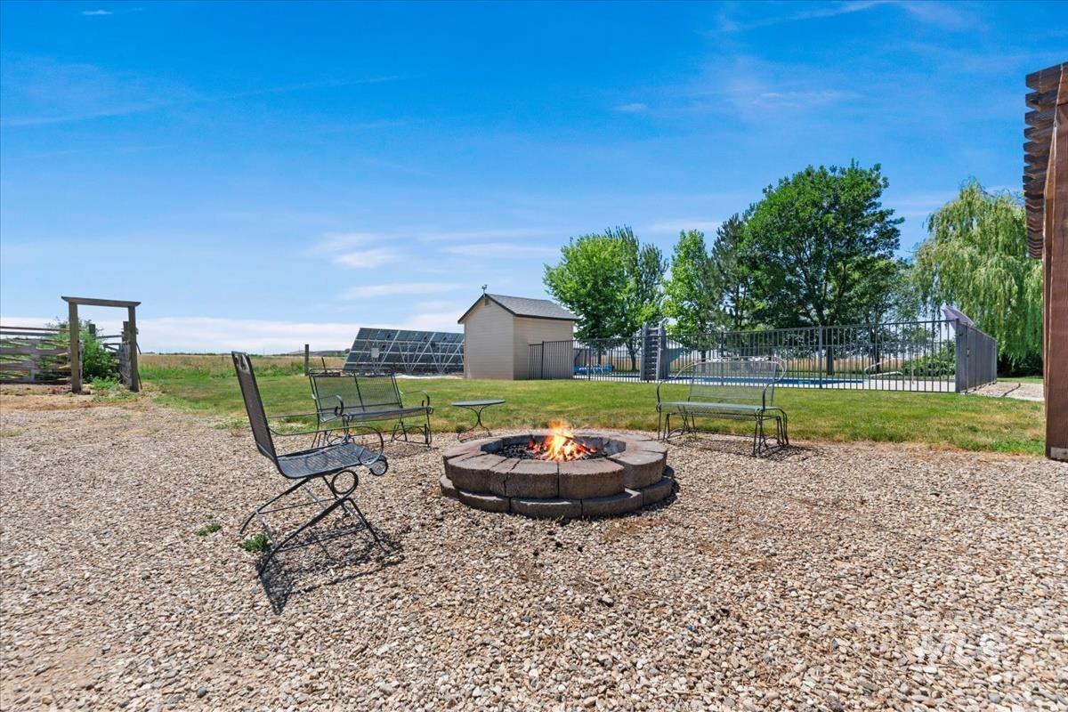 Gravel patio featuring a stone fire pit, wood pergola, and fenced outdoor pool