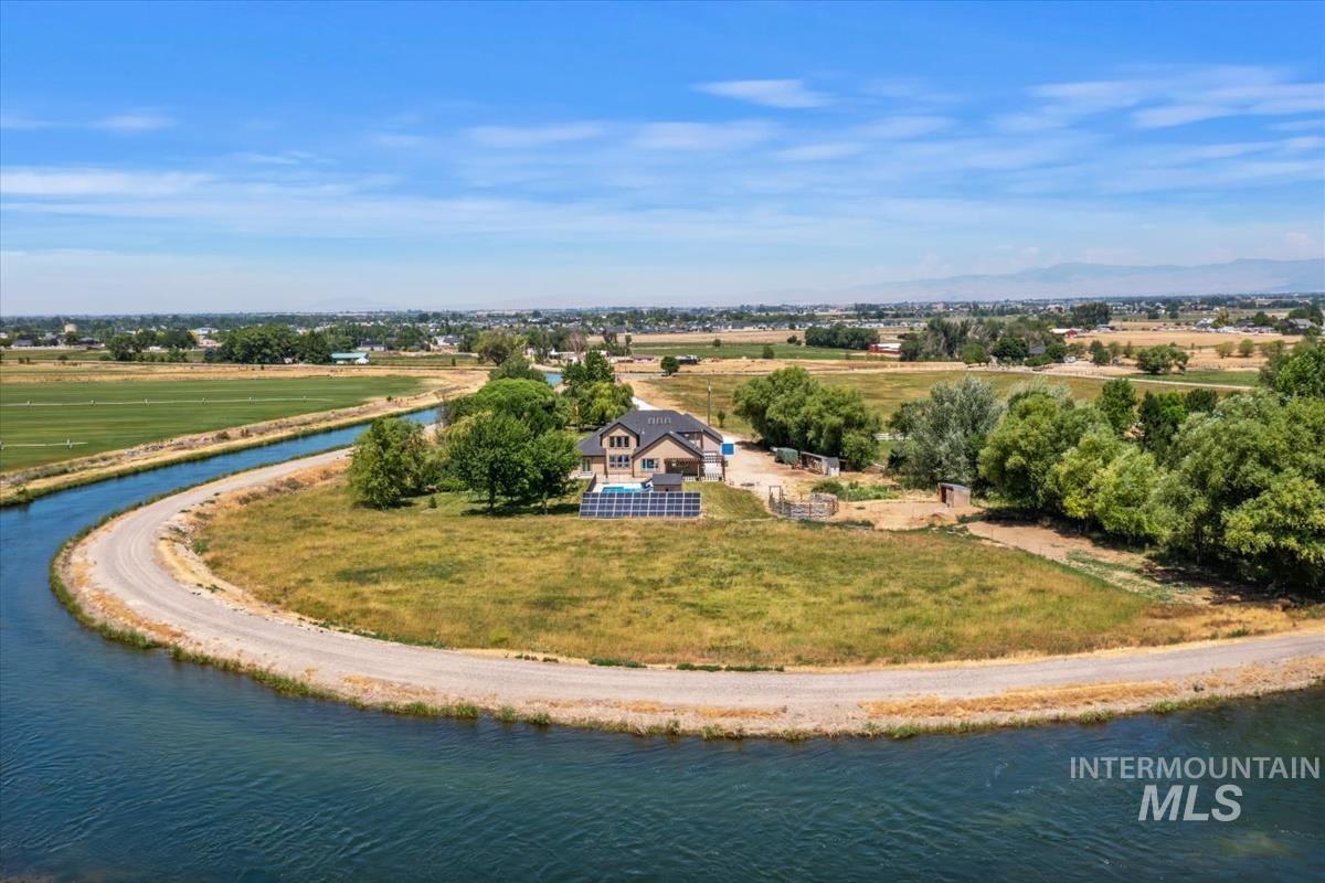 Expansive property featuring a single-family residence, a curved canal, mature trees, and solar panel arrays
