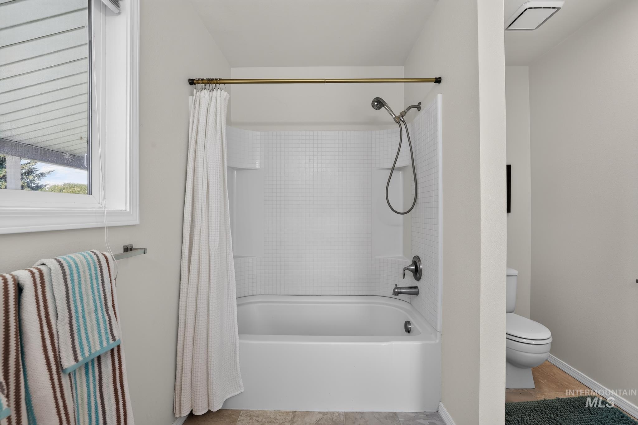 Bathtub and shower combination featuring a white tiled surround and brushed nickel fixtures