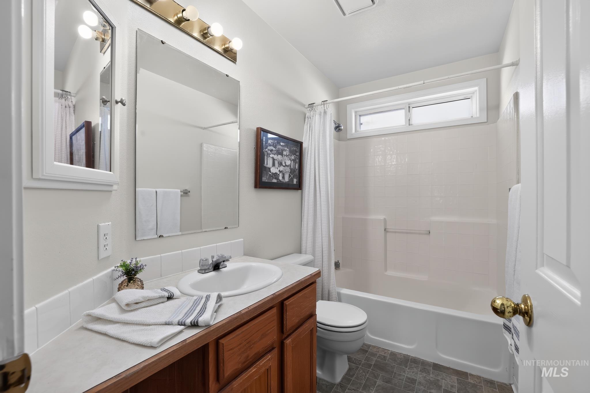 Bathroom featuring a wood-finish vanity with a white countertop and integrated sink, a large wall mirror, and a tub/shower combination with a transom window