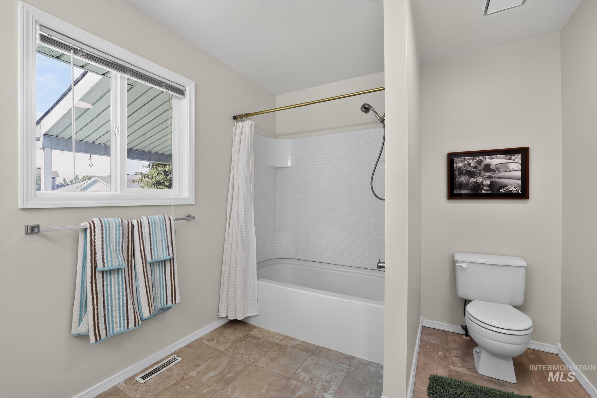 Bathroom featuring a shower-over-tub combination with a white subway tile surround, a single white toilet, a window with white trim, and a towel bar