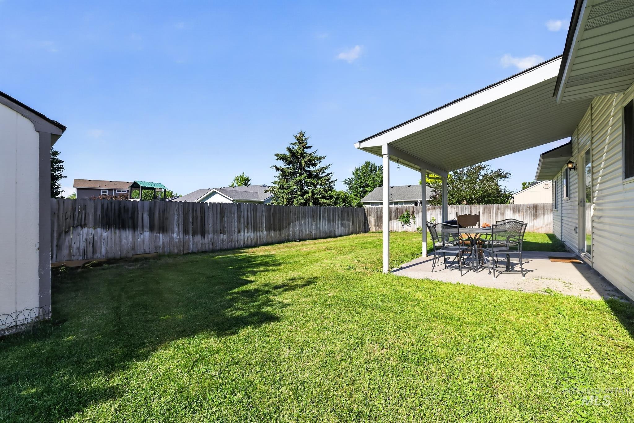 Expansive green lawn with a covered patio, concrete slab, and wood privacy fencing