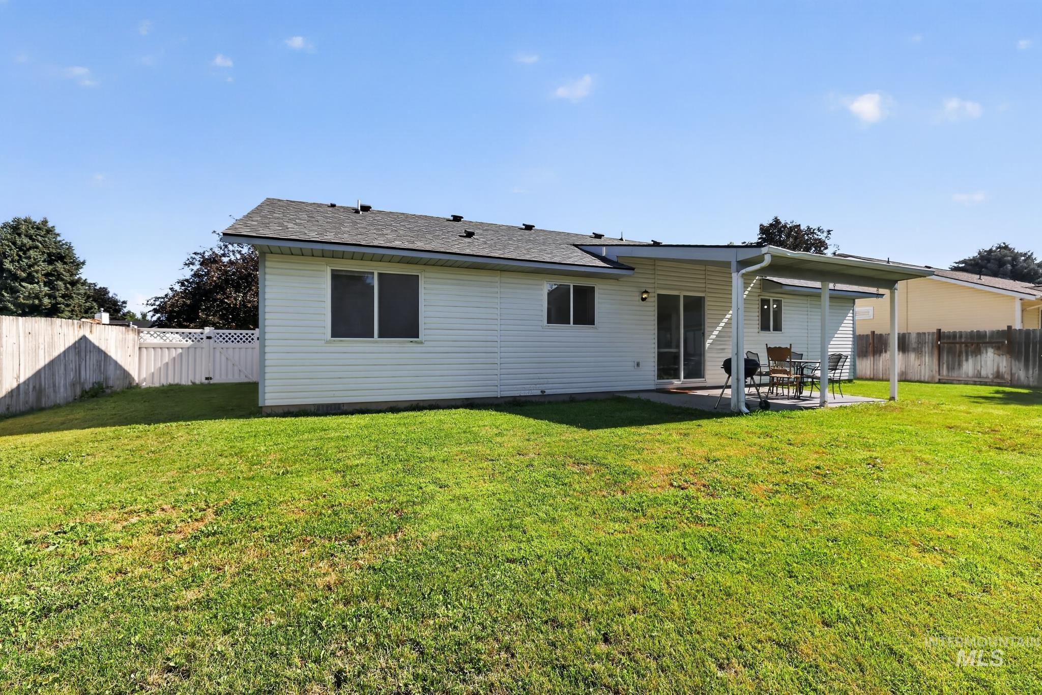 Expansive backyard featuring a lush lawn, white vinyl siding, a covered patio, and a sliding glass door entry