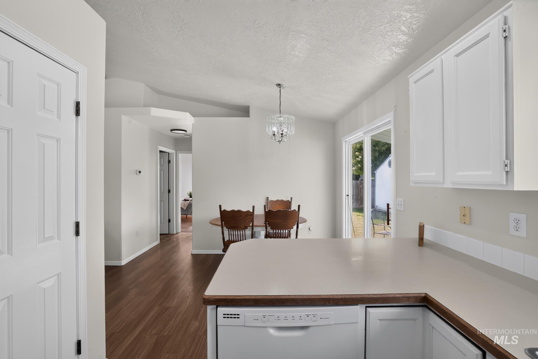 Kitchen featuring white cabinetry, light-toned countertops, a built-in dishwasher, and wood-finish flooring extending into the dining area