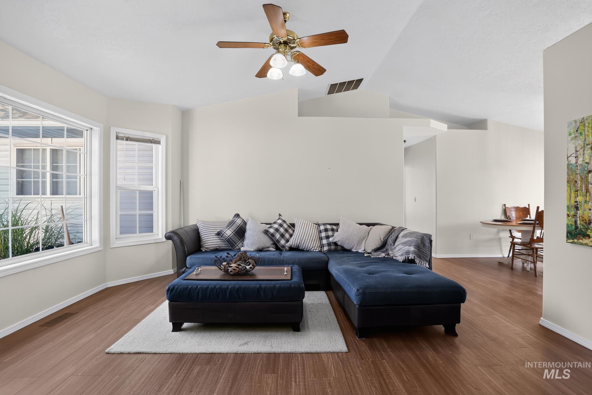 Spacious living area featuring wood-finish flooring, vaulted ceilings, and a ceiling fan with integrated lighting