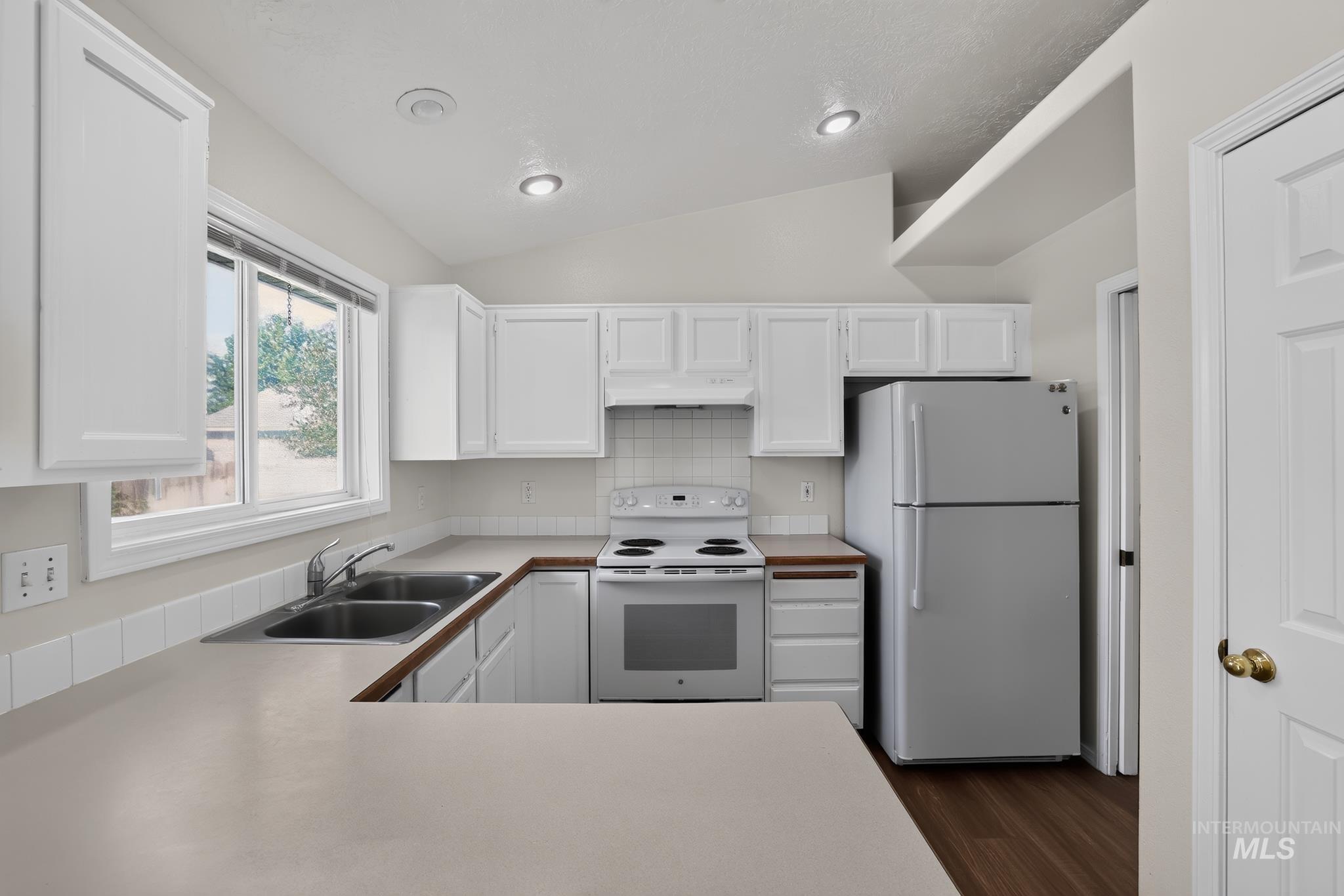Kitchen featuring white cabinetry, light-toned countertops, a double-basin stainless steel sink, a white electric range, and a stainless steel refrigerator
