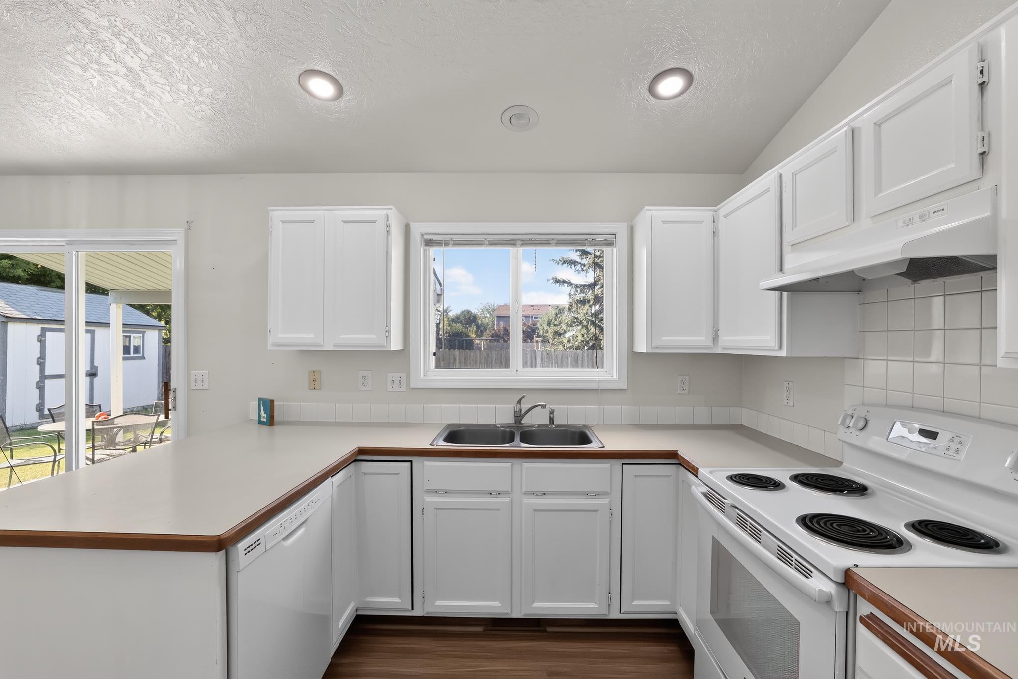 U-shaped kitchen featuring white cabinetry, light countertops with wood-finish trim, a double basin sink, and a built-in range and oven