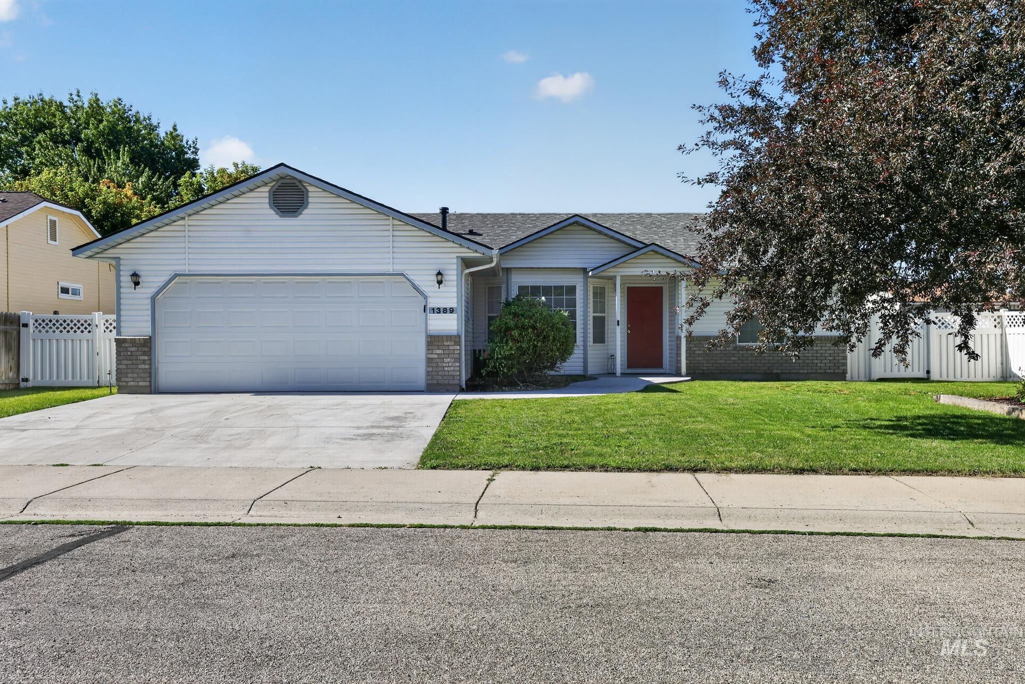 Ranch-style exterior featuring light-colored siding, a prominent attached garage with a concrete driveway, a vibrant red front door, and a manicured front lawn