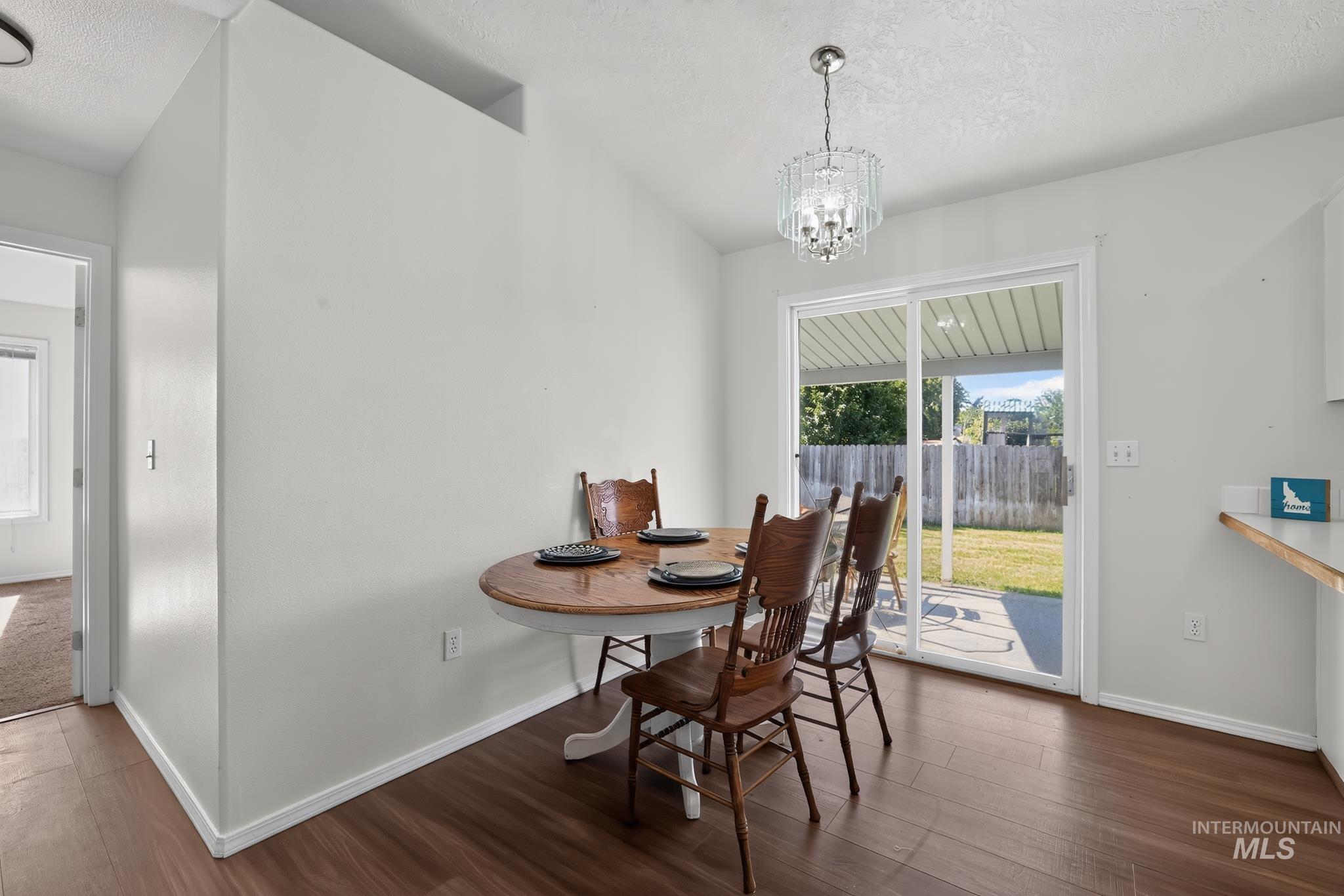 Dining area featuring wood-finish flooring, a contemporary chandelier, and direct access to the outdoor patio and fenced backyard via sliding glass doors