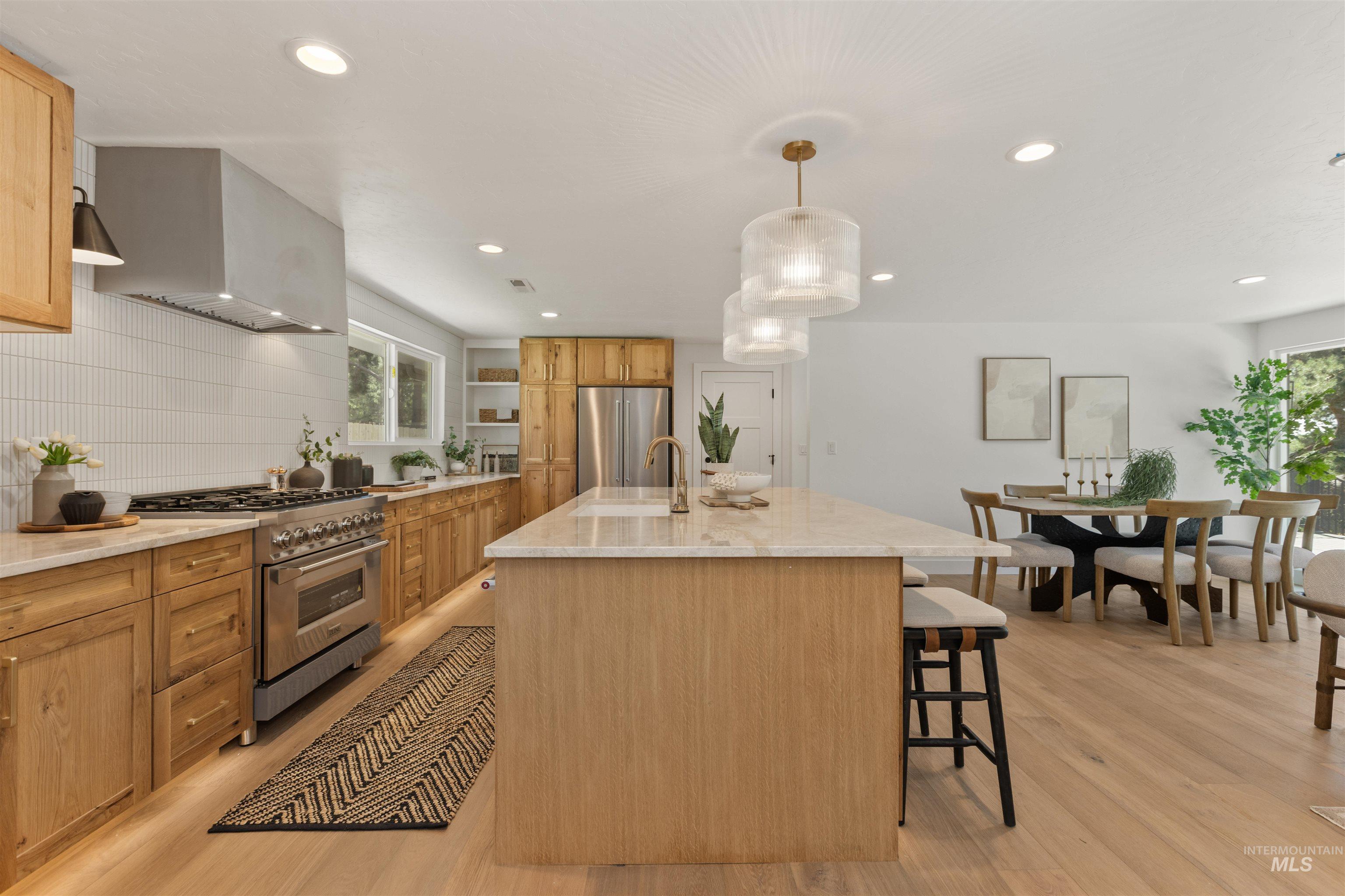 Kitchen featuring high end appliances, an island with sink, plenty of natural light, wall chimney exhaust hood, and recessed lighting