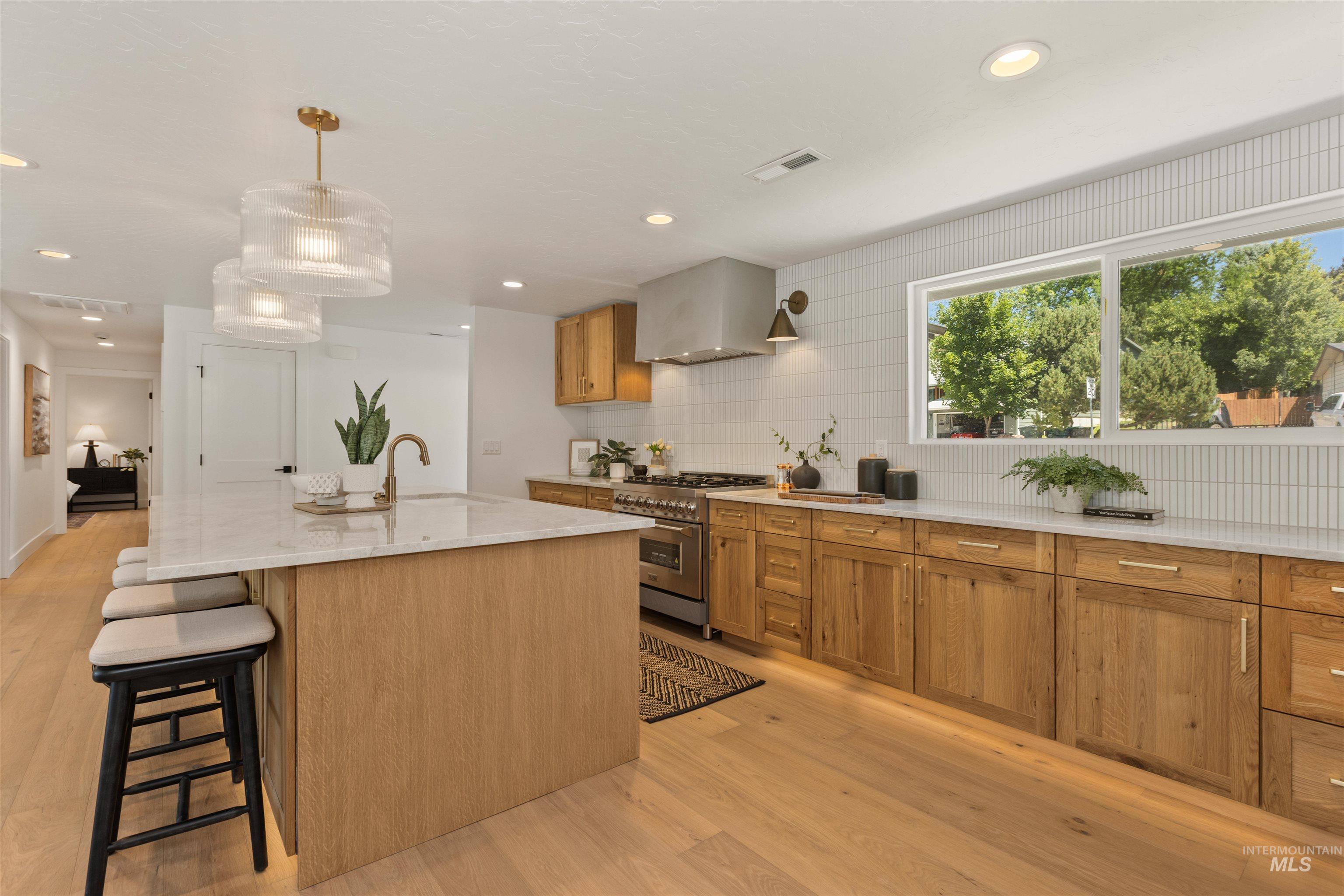 Kitchen with wall chimney range hood, stainless steel range, a breakfast bar, hanging light fixtures, and light wood finished floors