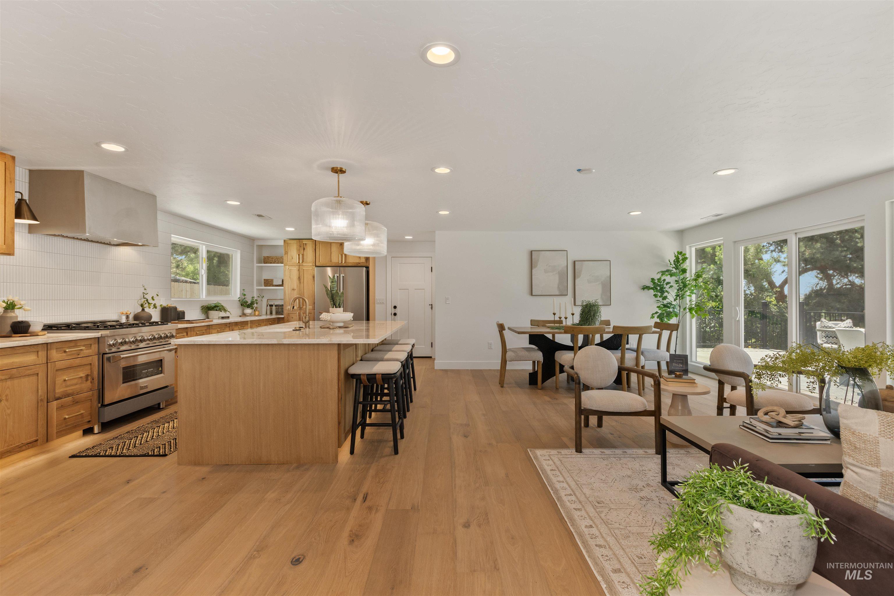 Kitchen with an island with sink, high end appliances, hanging light fixtures, recessed lighting, and light wood-style floors