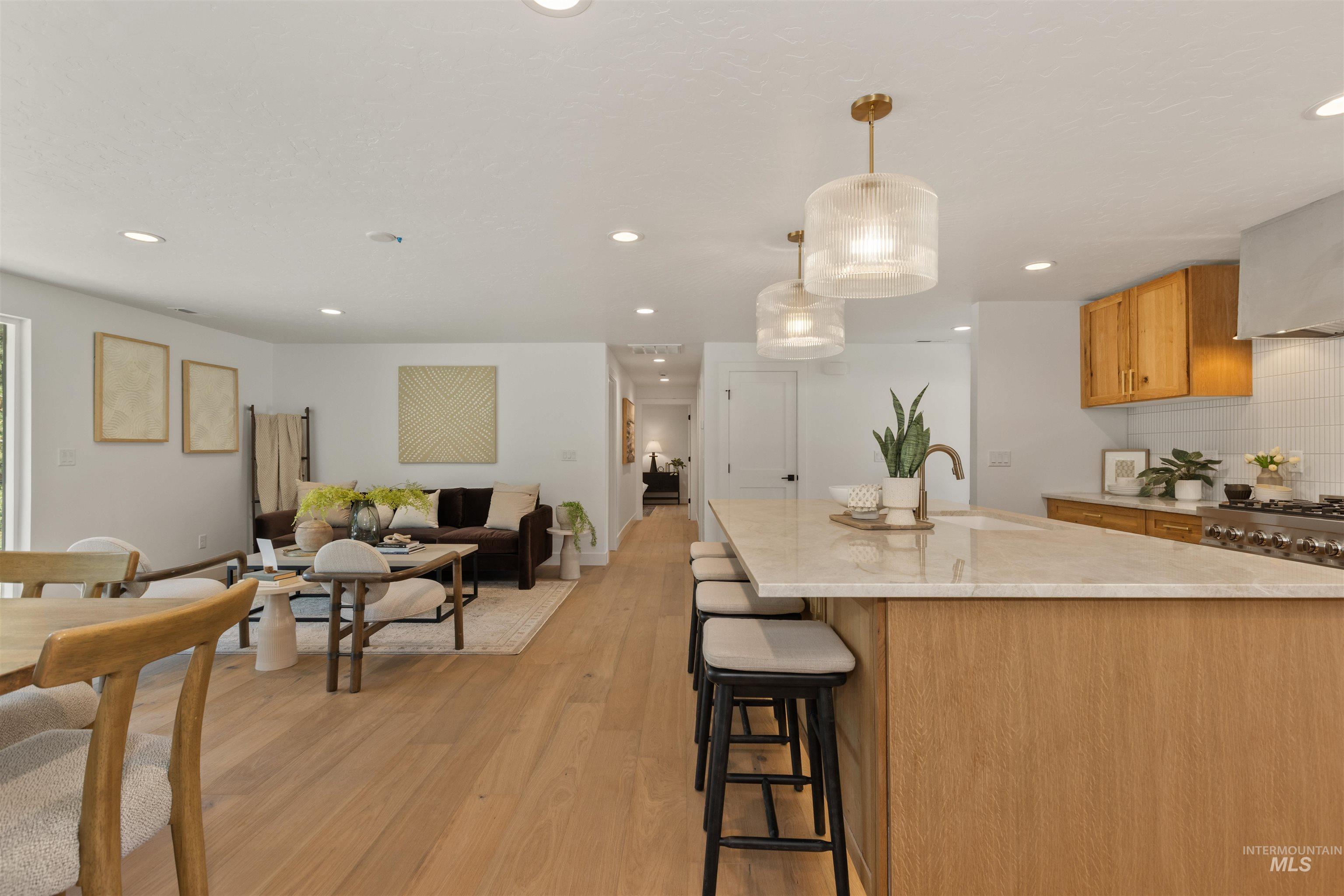 Kitchen featuring light wood finished floors, decorative light fixtures, a kitchen bar, decorative backsplash, and open floor plan