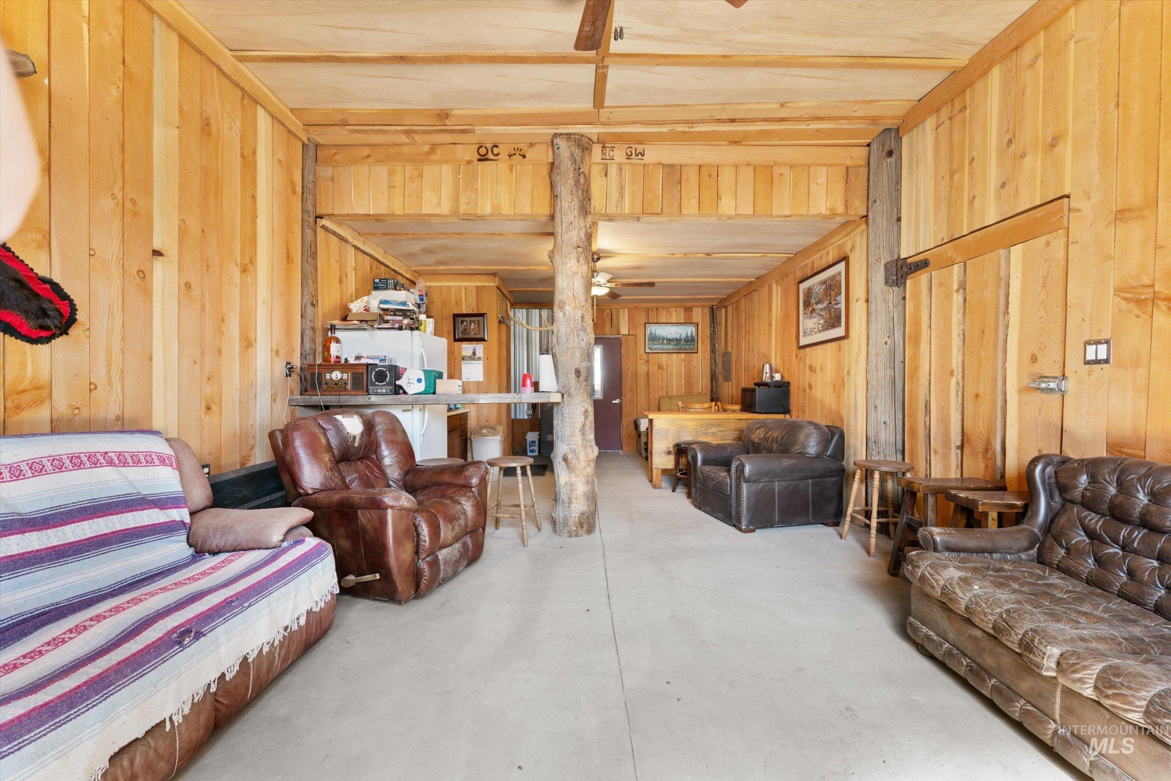 Living area featuring concrete floors, ceiling fan, and wooden walls