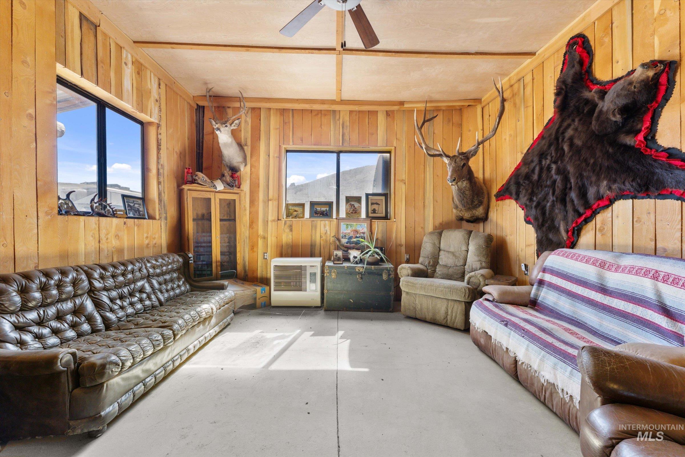 Living area featuring heating unit, ceiling fan, concrete floors, and wooden walls