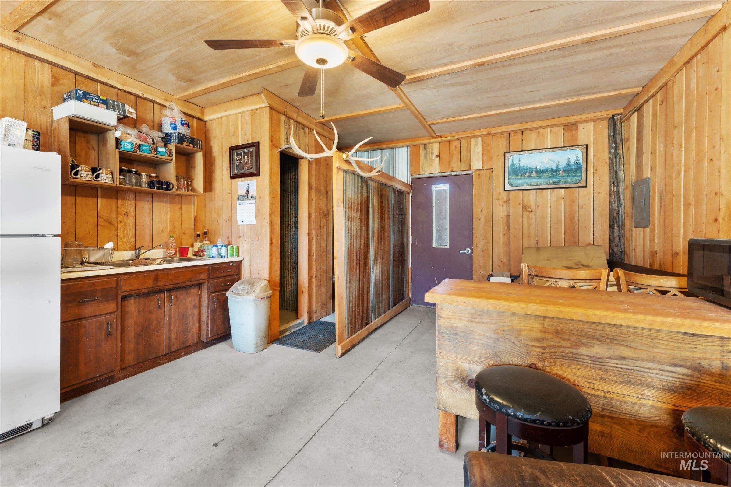 Kitchen with concrete flooring, freestanding refrigerator, light countertops, wood walls, and open shelves