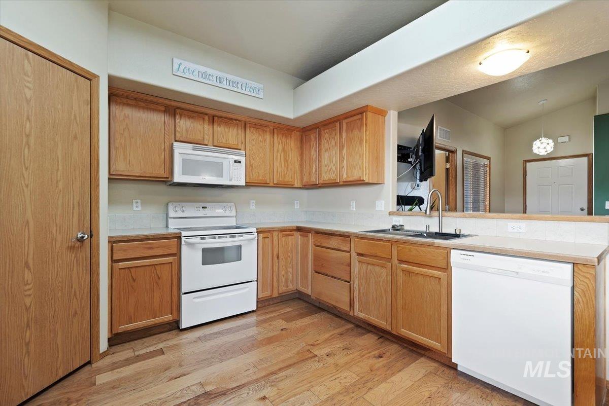 Kitchen featuring white appliances, light countertops, light wood-style floors, pendant lighting, and a peninsula