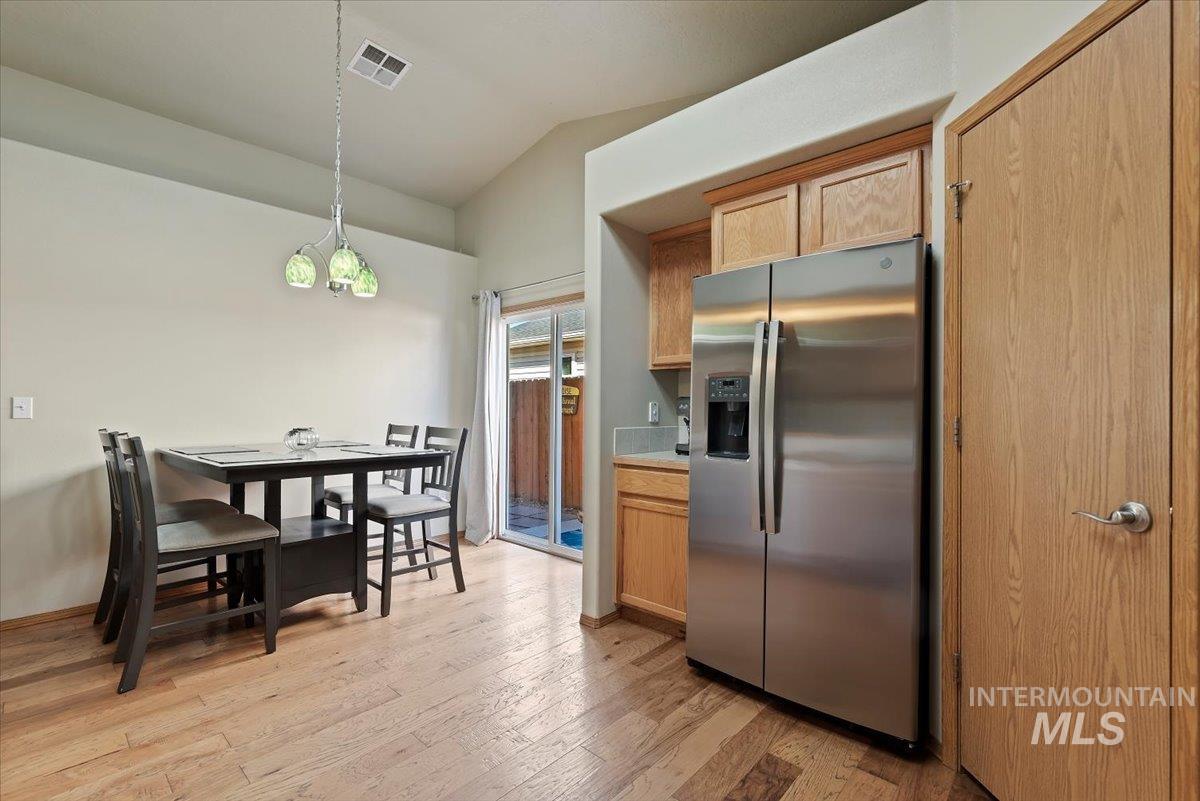 Kitchen with stainless steel fridge with ice dispenser, light wood finished floors, hanging light fixtures, lofted ceiling, and light countertops