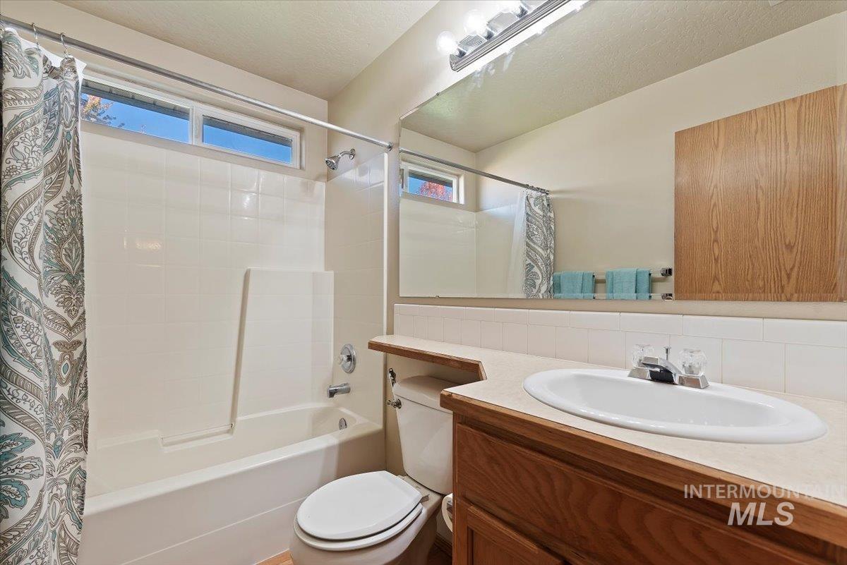 Full bath with vanity, shower / tub combo with curtain, tasteful backsplash, and a textured ceiling