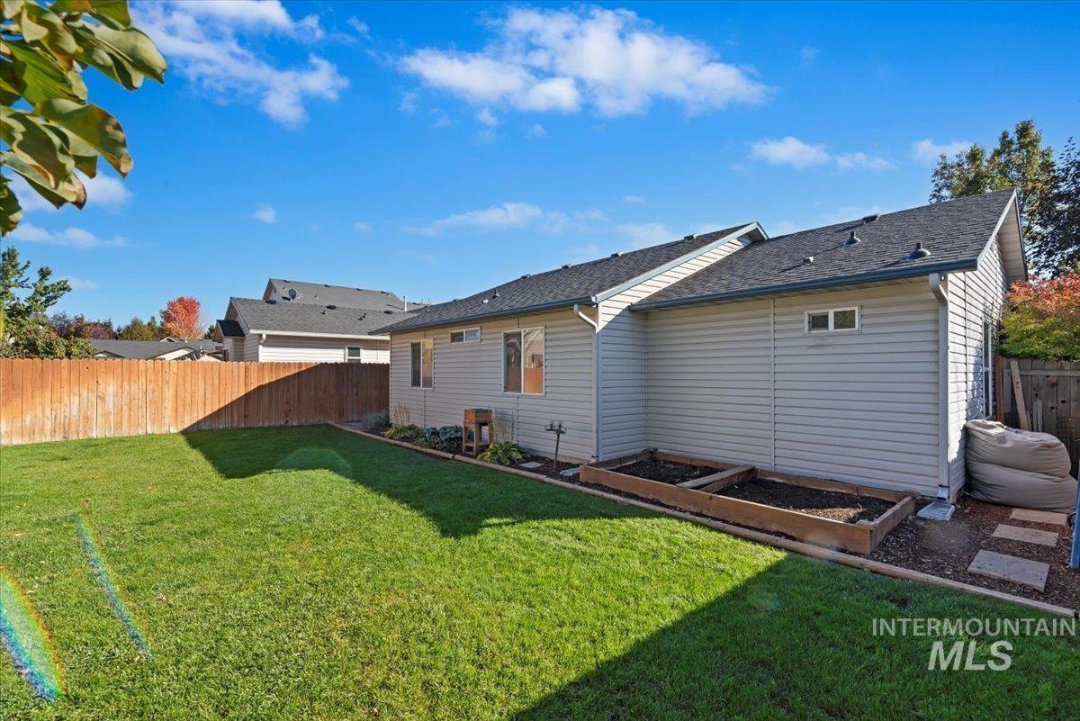 Back of house featuring a vegetable garden, a fenced backyard, and a shingled roof