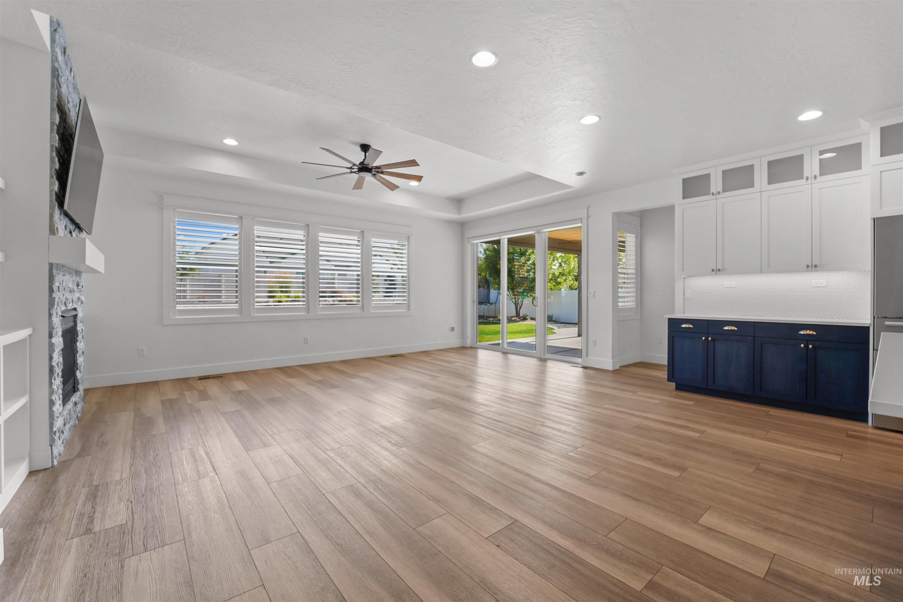 Unfurnished living room featuring a ceiling fan, recessed lighting, light wood-style floors, and a raised ceiling