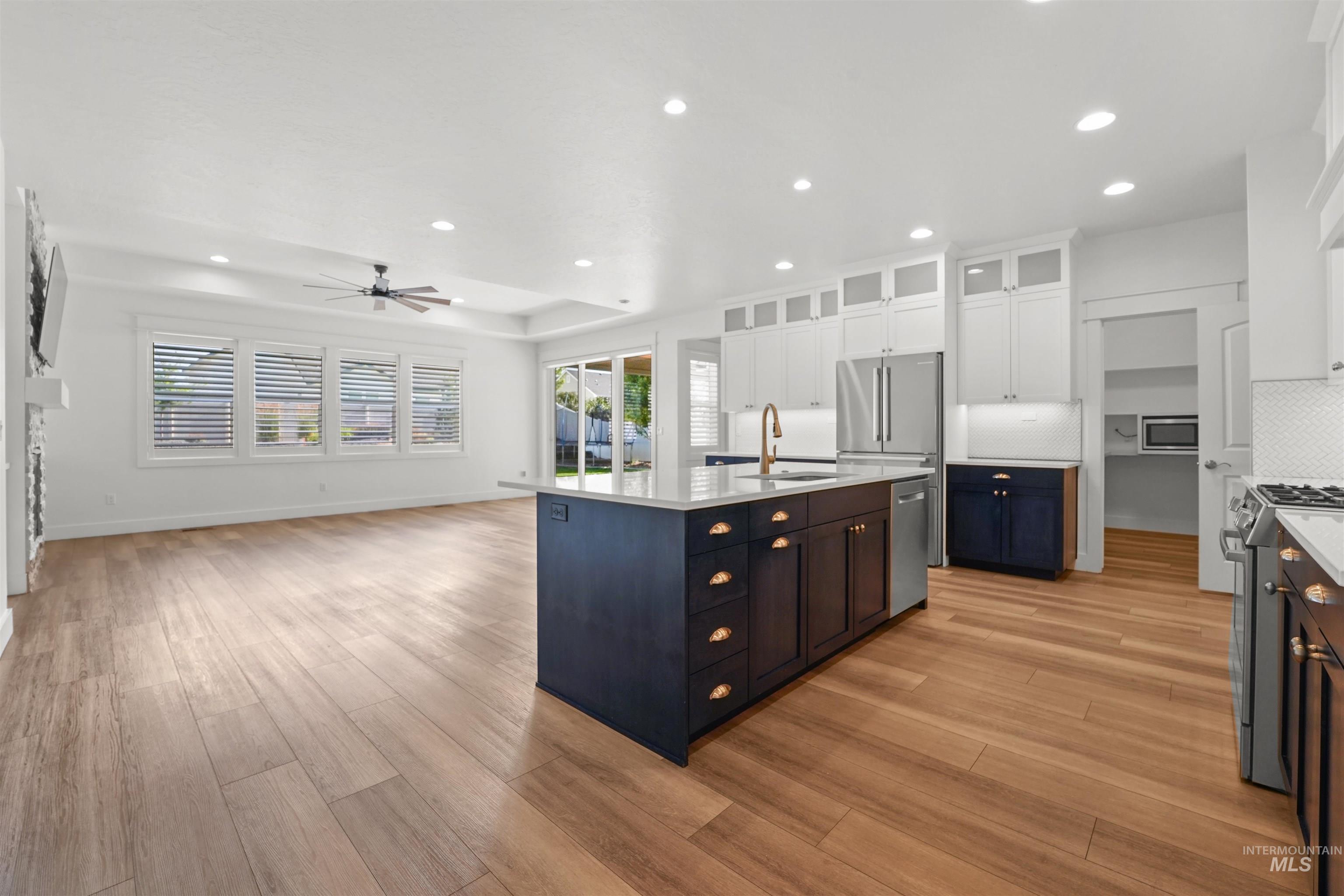 Kitchen with stainless steel appliances, light countertops, ceiling fan, white cabinets, and light wood-style flooring