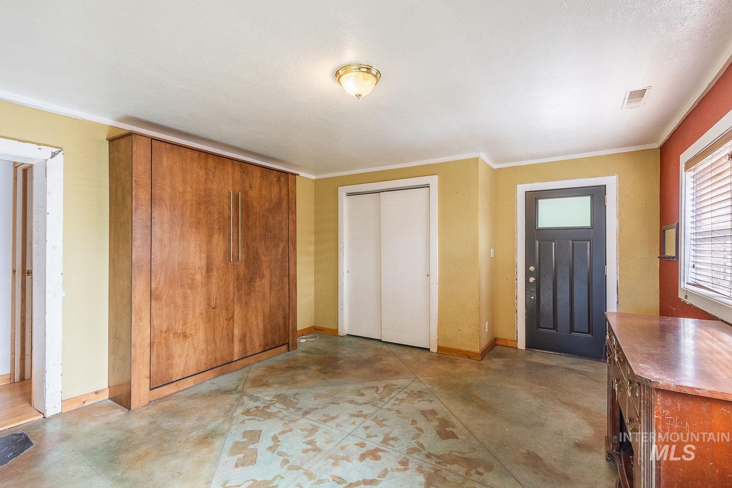 Room featuring a built-in wood-finish wall bed, stained concrete flooring, and a dark paneled door with a rectangular lite
