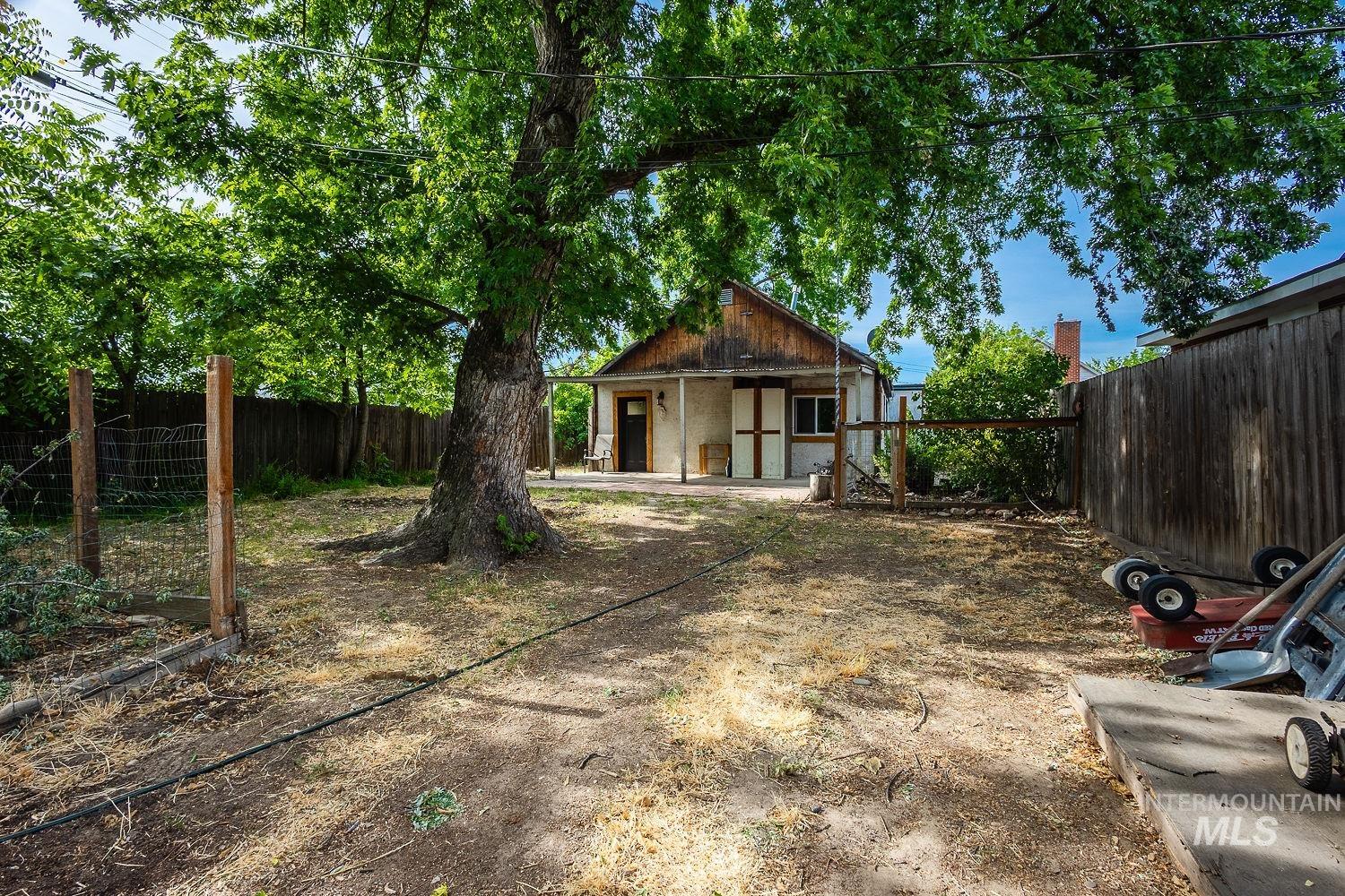 Fenced backyard with mature trees providing shade and a separate structure featuring a shed roof and double doors