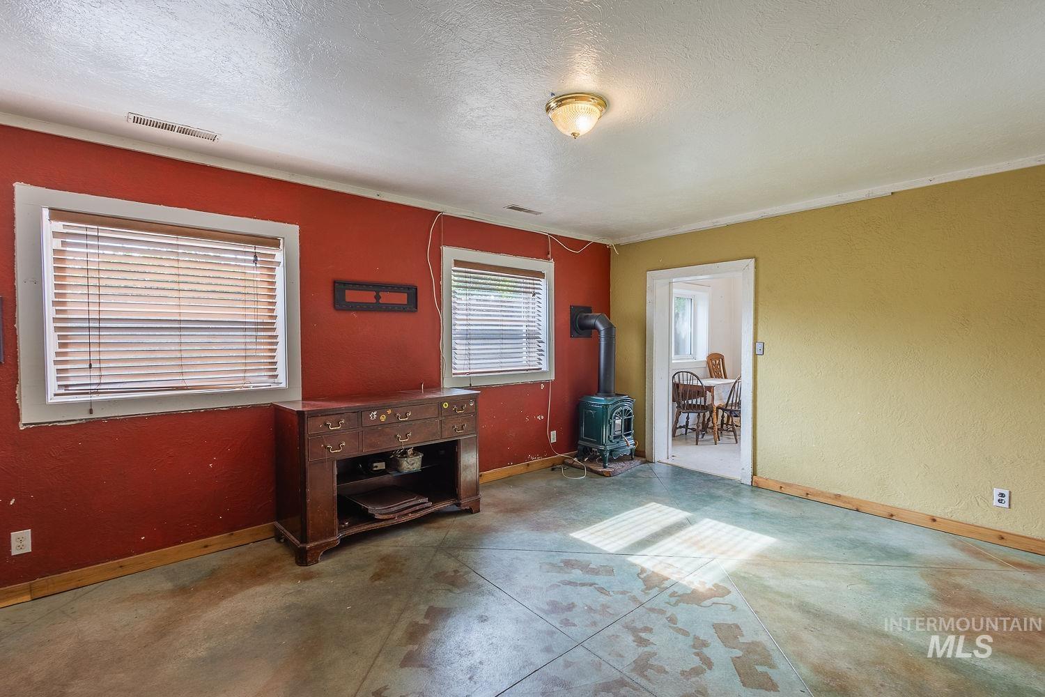 Spacious room featuring multiple windows with blinds, a wood-burning stove, and a doorway opening to an additional room