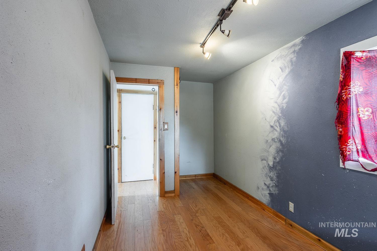 Interior room featuring wood-finish flooring, a white interior door with brass hardware, and track lighting