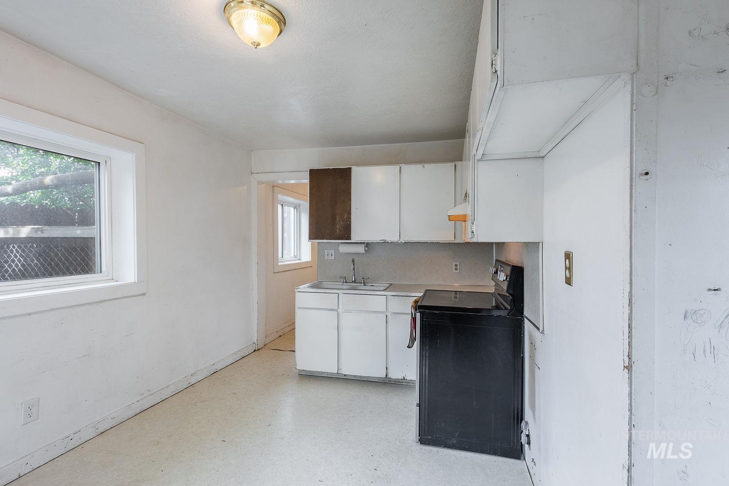 Functional kitchen area featuring white cabinetry, a compact sink, and a black freestanding range