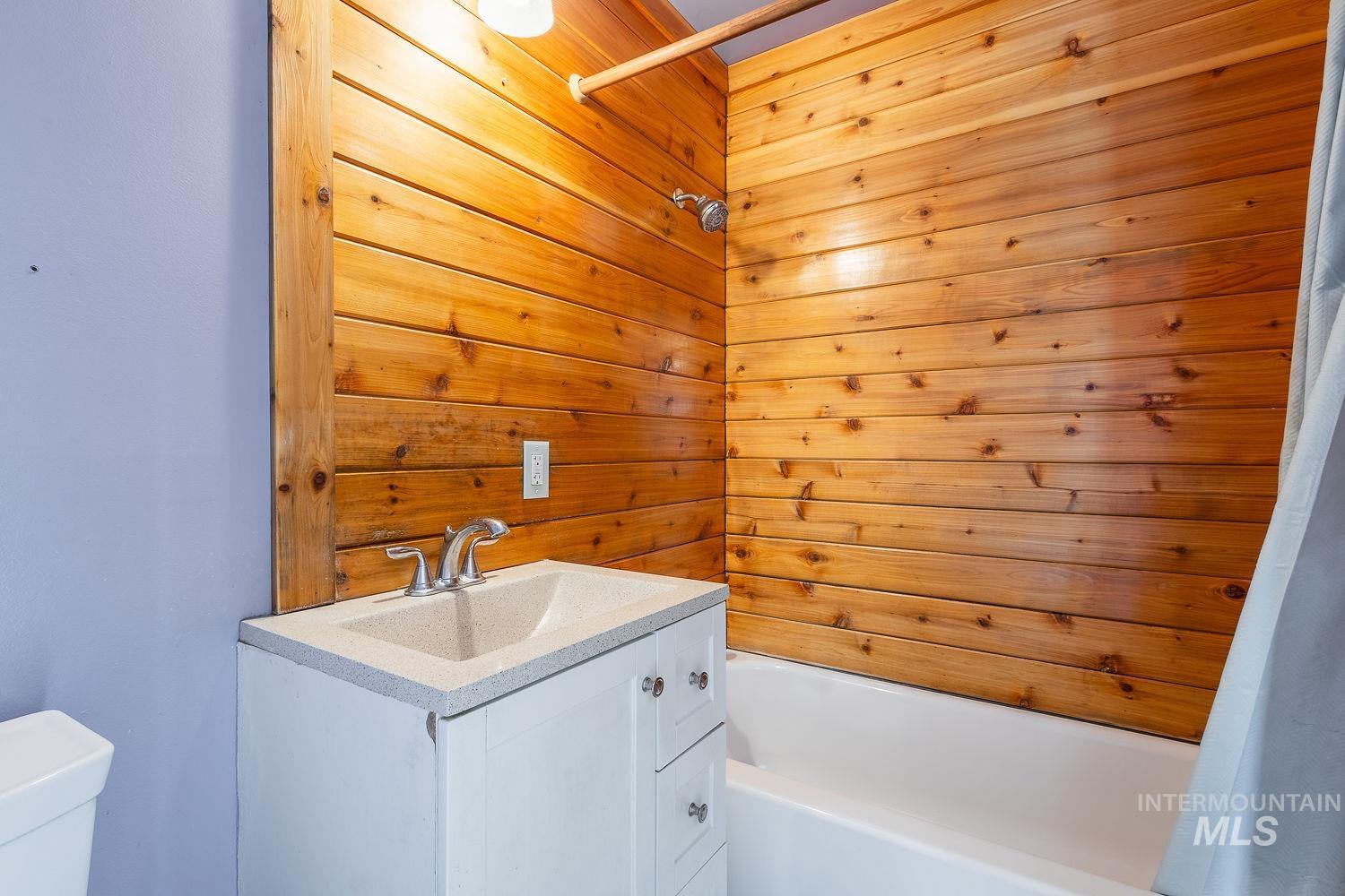 Bathroom featuring a wood-panel accent wall and a white vanity with an integrated sink