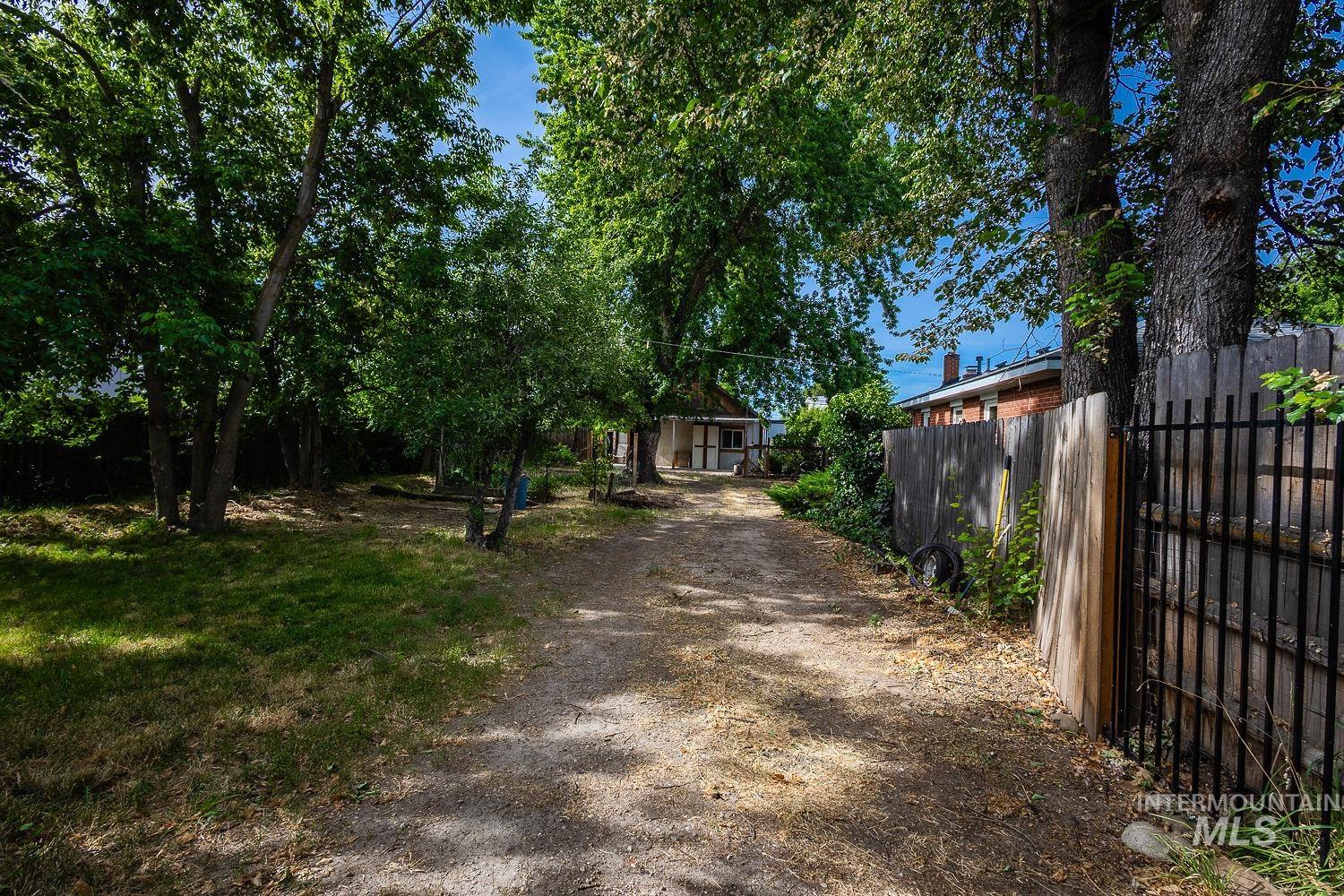Gravel driveway framed by mature trees and a wooden privacy fence with an iron gate