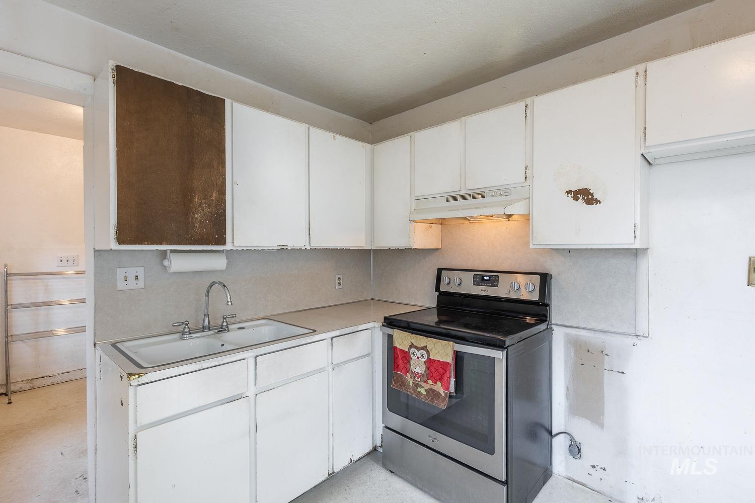 Kitchen area featuring white cabinetry, a double-basin sink with a chrome faucet, a stainless steel electric range, and laminate countertops