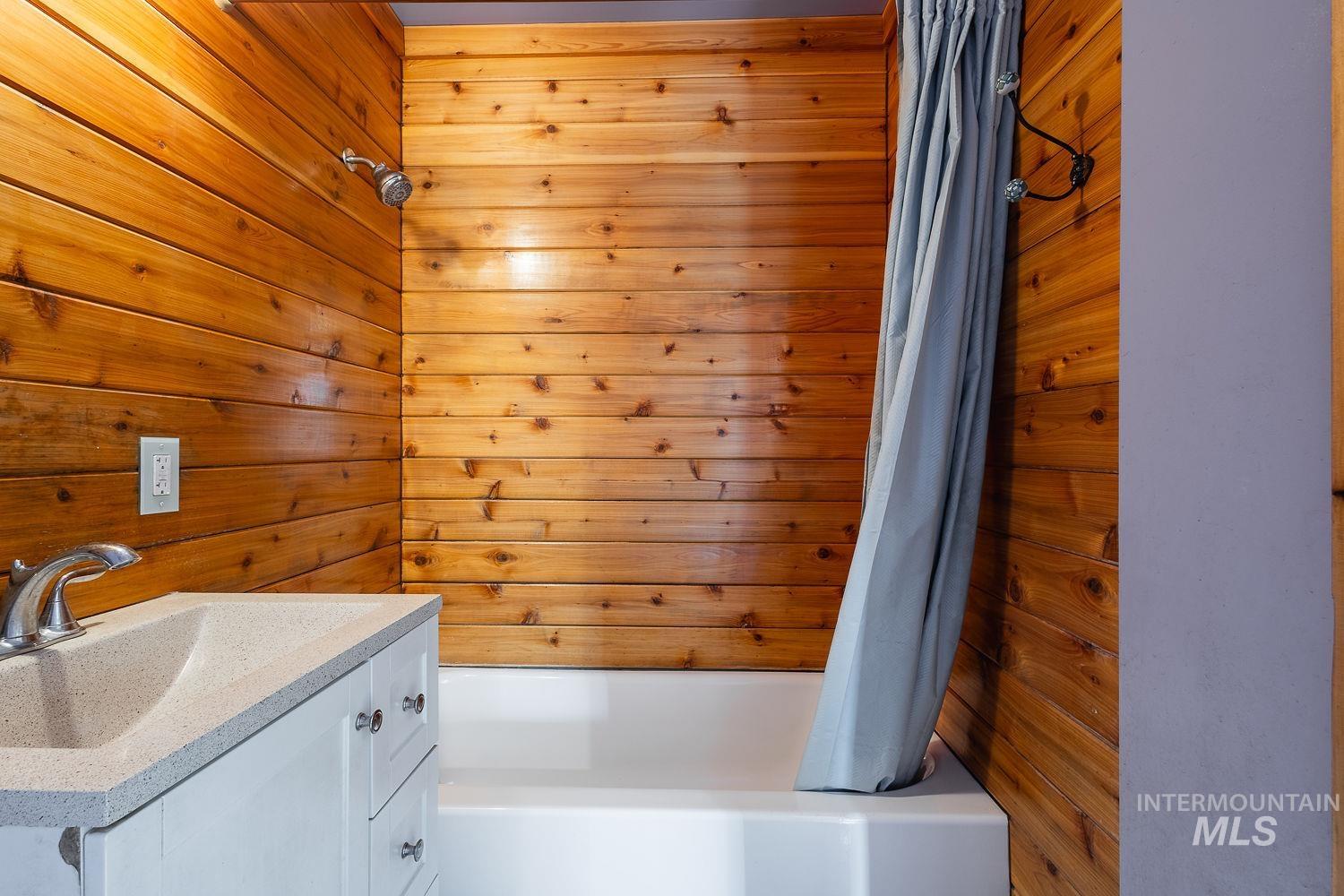 Bathroom featuring wood-paneled walls, a white bathtub, and a modern vanity with an integrated sink and chrome faucet
