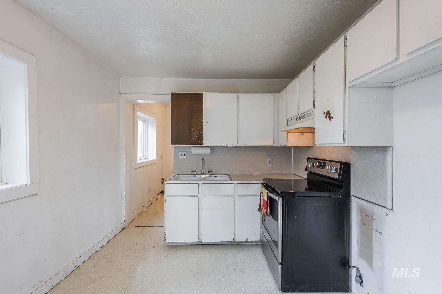 Kitchen area with white cabinetry, a double basin sink, and a black electric range