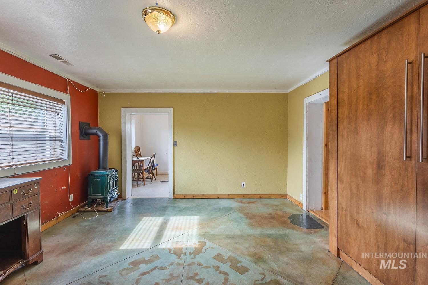 Interior space featuring a freestanding wood-burning stove, concrete flooring, built-in wood-finish cabinetry, and a window with blinds