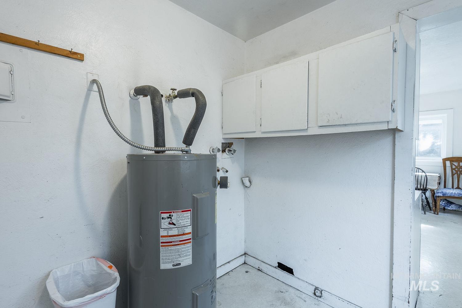 Utility space featuring a water heater, white cabinetry, and white painted walls