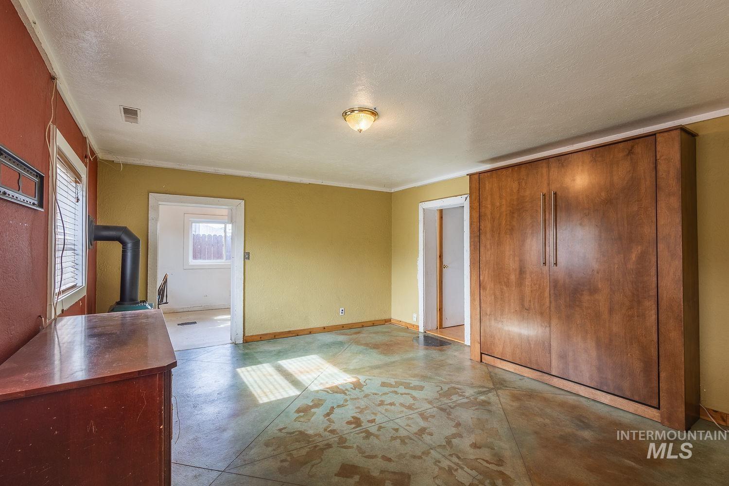 Spacious room featuring a built-in wood-finish cabinet, a wood-burning stove with a black pipe, and concrete flooring