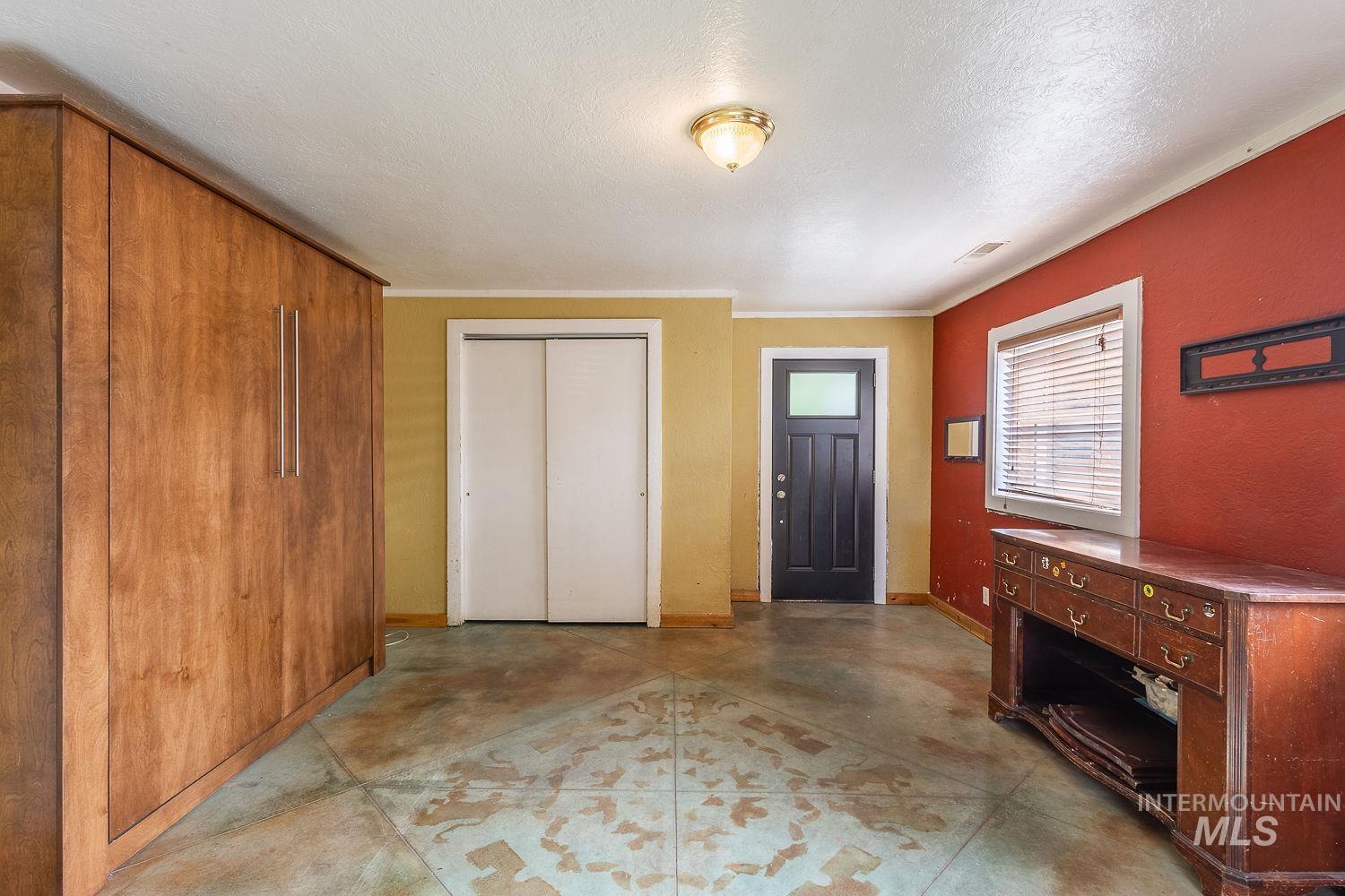 Spacious room featuring a dark wood-finish built-in wall unit, patterned concrete flooring, white bi-fold closet doors, and a solid black entry door with a frosted glass panel
