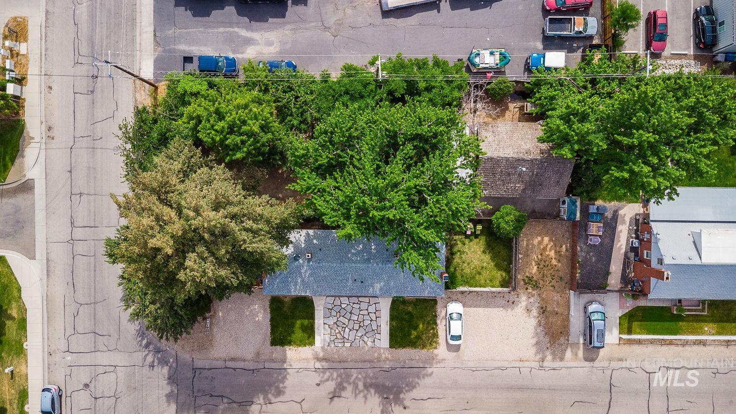 Aerial property perspective showcasing a residential structure with a dark shingle roof, a stone pathway, and a gravel driveway