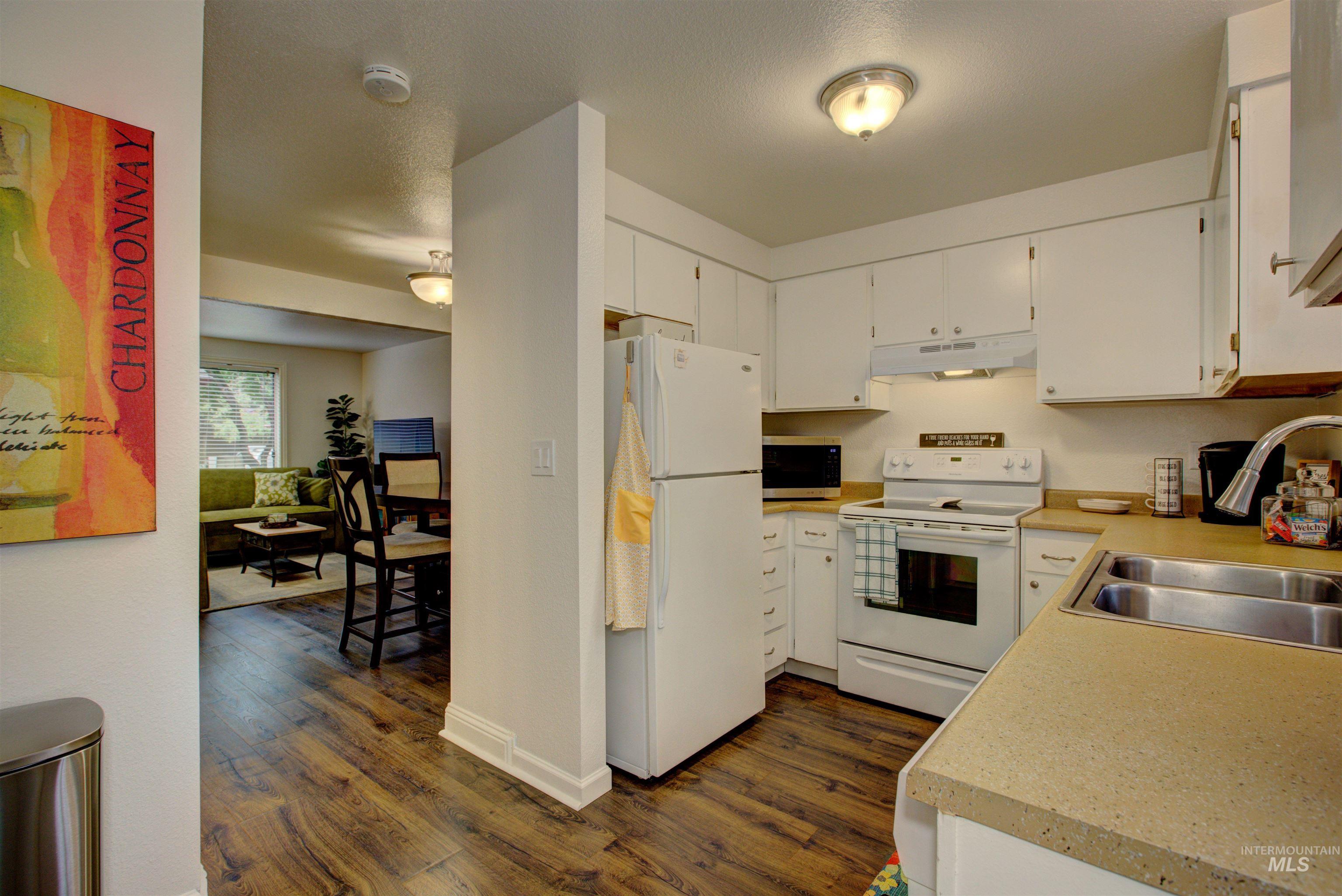 Kitchen with white appliances, dark wood-type flooring, under cabinet range hood, light countertops, and white cabinets