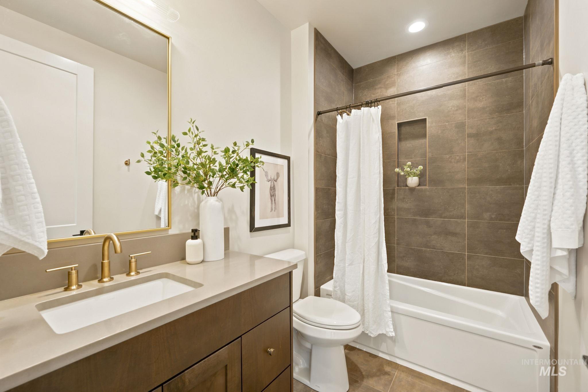 Bathroom featuring a single vanity with a light-colored countertop and undermount sink, a gold-toned faucet, and a frameless gold-toned mirror