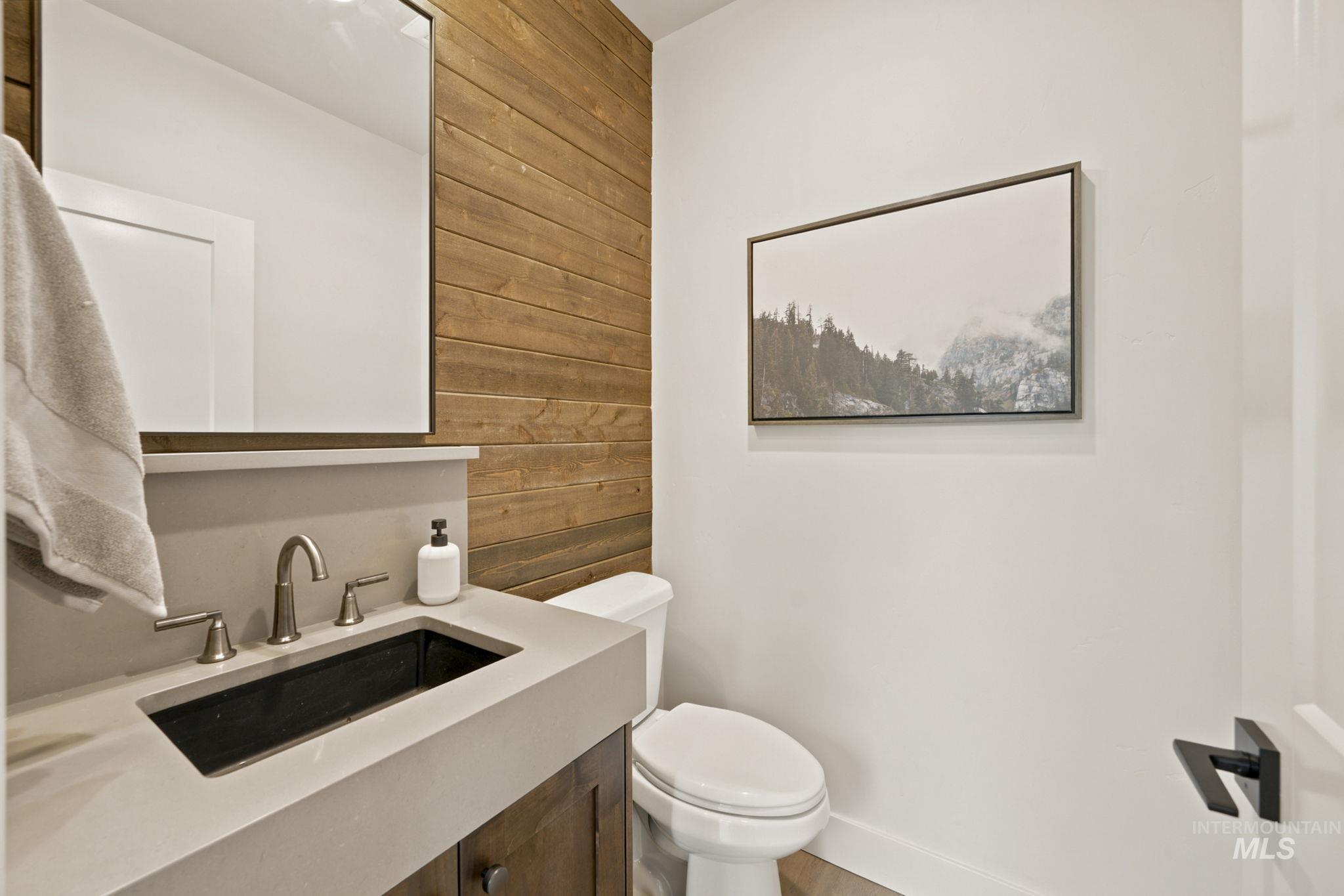 Powder room featuring a wood plank accent wall, a rectangular mirror, and a vanity with an integrated sink and brushed nickel faucet - Powder Bath Main Floor