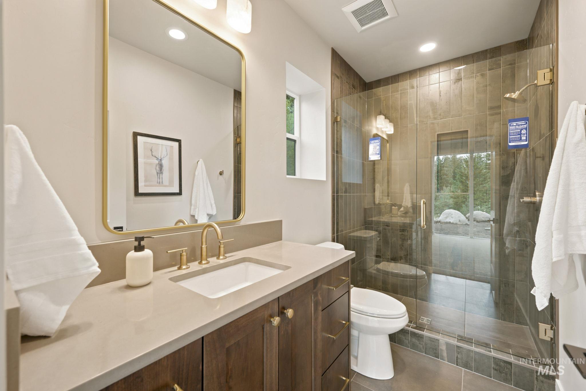 Modern bathroom featuring a wood-finish vanity with a light countertop, gold-finish faucet, and coordinating framed mirror