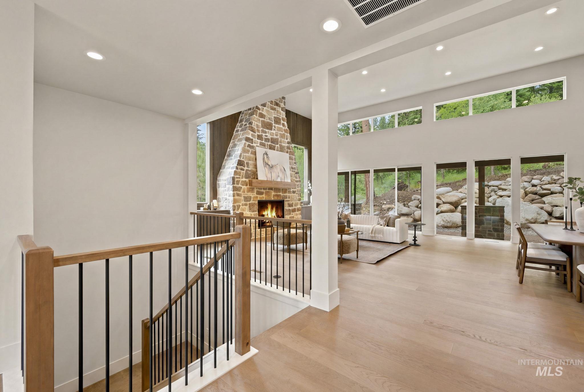 Expansive open-concept living area featuring a stone-clad fireplace, high ceilings, wood-finish flooring, and a wall of glass doors and transom windows - Second Floor
