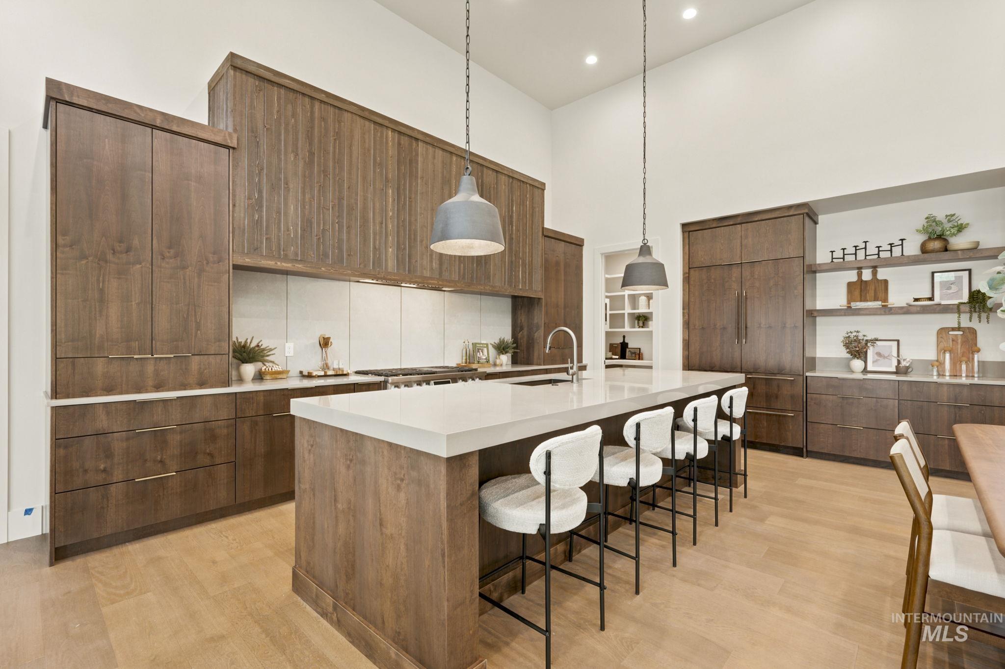 Kitchen featuring light wood-finish flooring, a large island with a light-toned countertop, integrated refrigeration, a light backsplash, and wood cabinetry