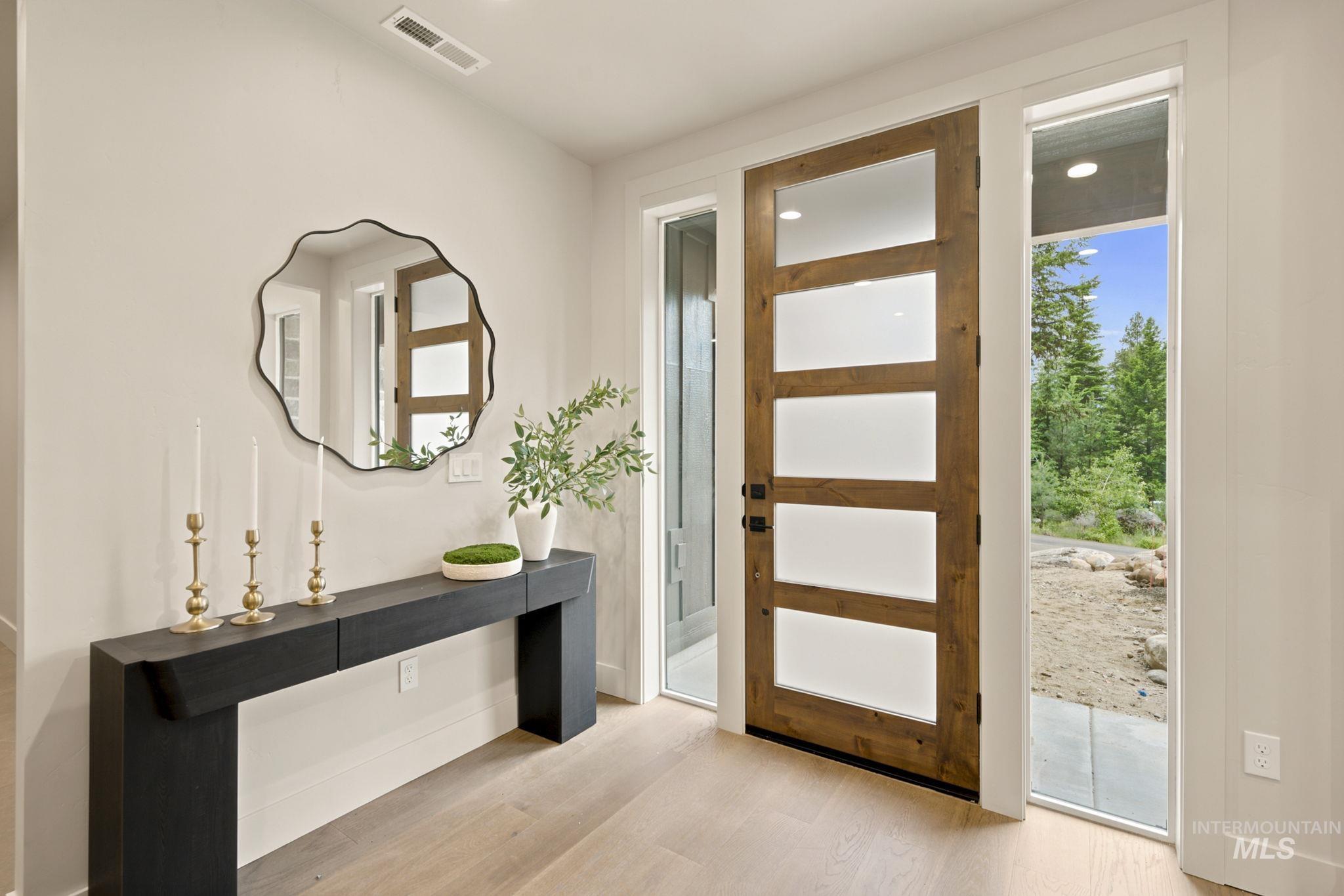 Entryway featuring a modern wood-paneled door with frosted glass inserts, light wood-finish flooring, a contemporary console table, and a decorative wall mirror - Main Floor Front Door