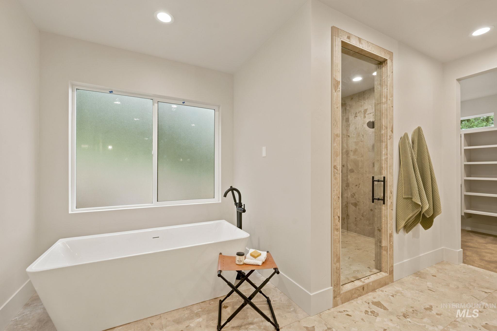 Freestanding soaking tub with a floor-mounted matte black faucet, frosted window, walk-in shower with glass enclosure, and built-in shelving - Primary Second Floor
