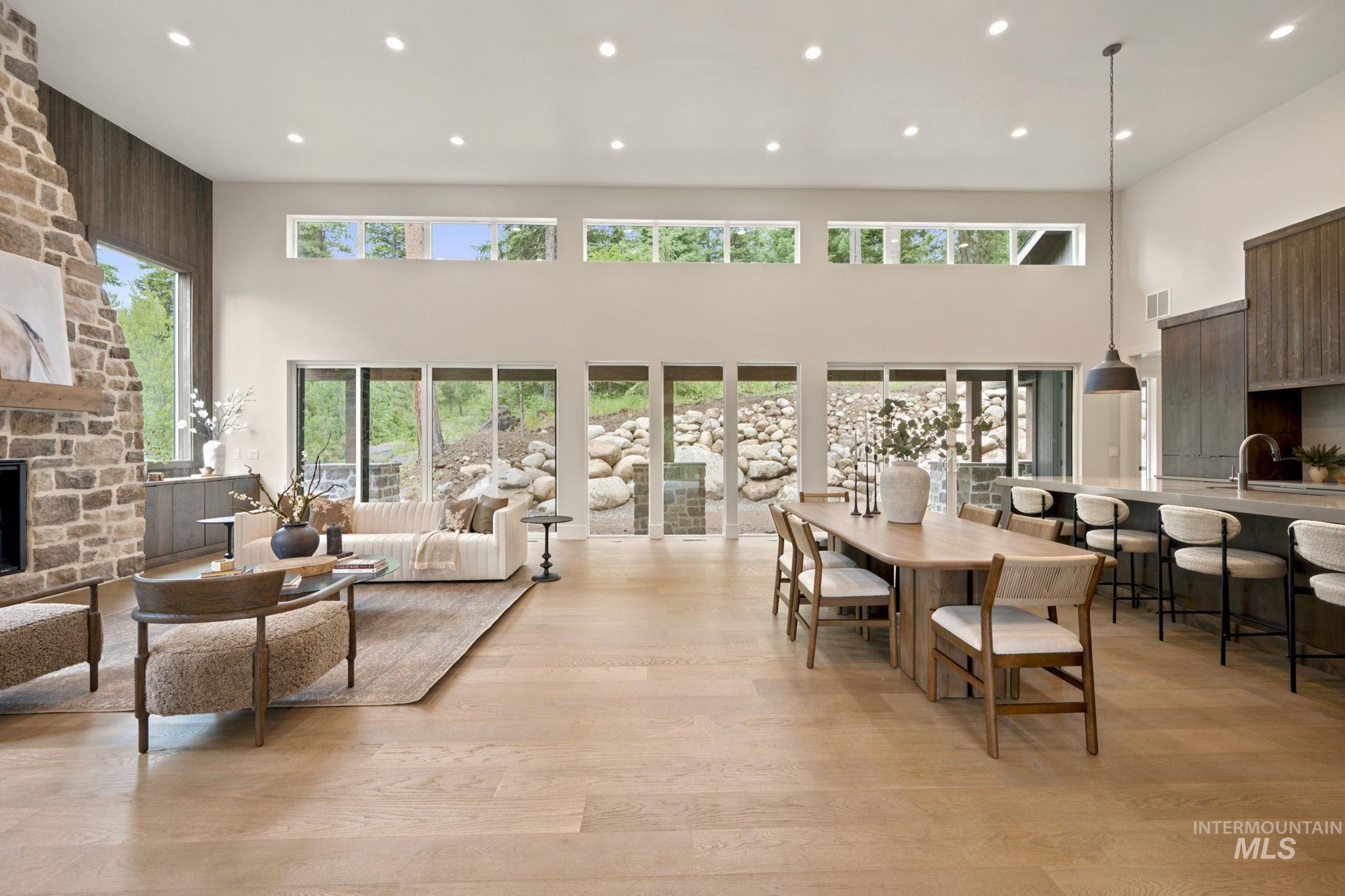 Expansive great room featuring light wood-finish flooring, a stone fireplace with a wood mantle, and a high ceiling with recessed lighting